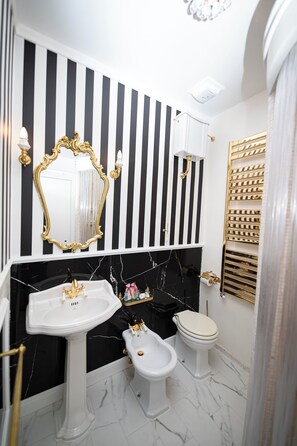 A bathroom with a black and white striped wall, a gold-framed mirror, a pedestal sink, a toilet, and a gold-framed shelf with toiletries. - guest house eros suite (Rome)