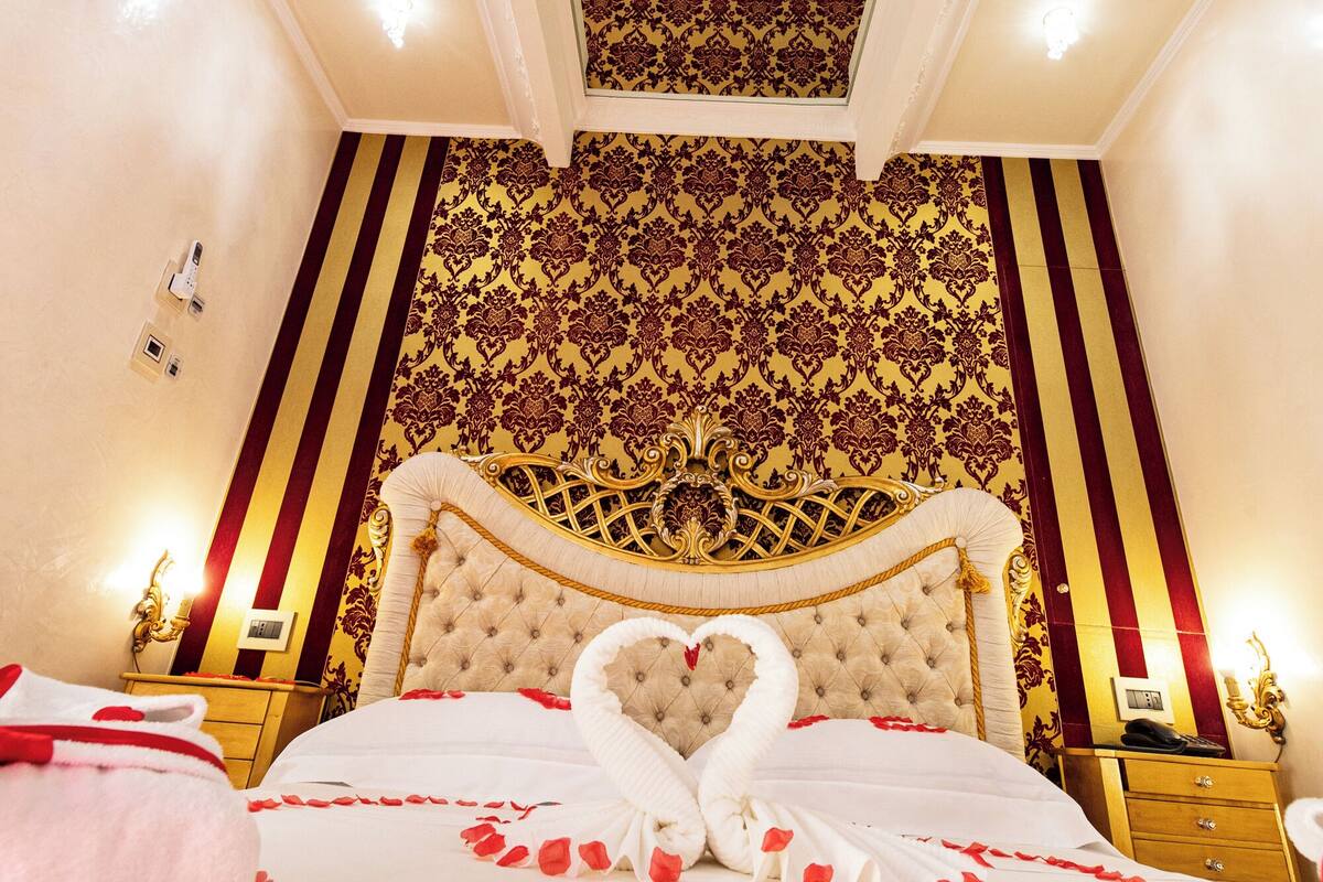 A luxurious bedroom with a large bed, ornate headboard, and a decorative ceiling.