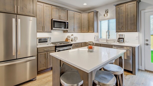 Una cocina moderna con electrodomésticos de acero inoxidable, armarios de madera y una isla central con taburetes de bar.