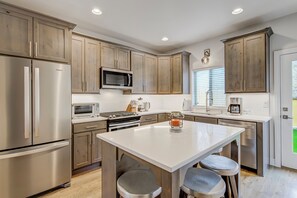 A modern kitchen with stainless steel appliances, wooden cabinets, and a central island with bar stools. - The Chestnut (Colorado Springs)