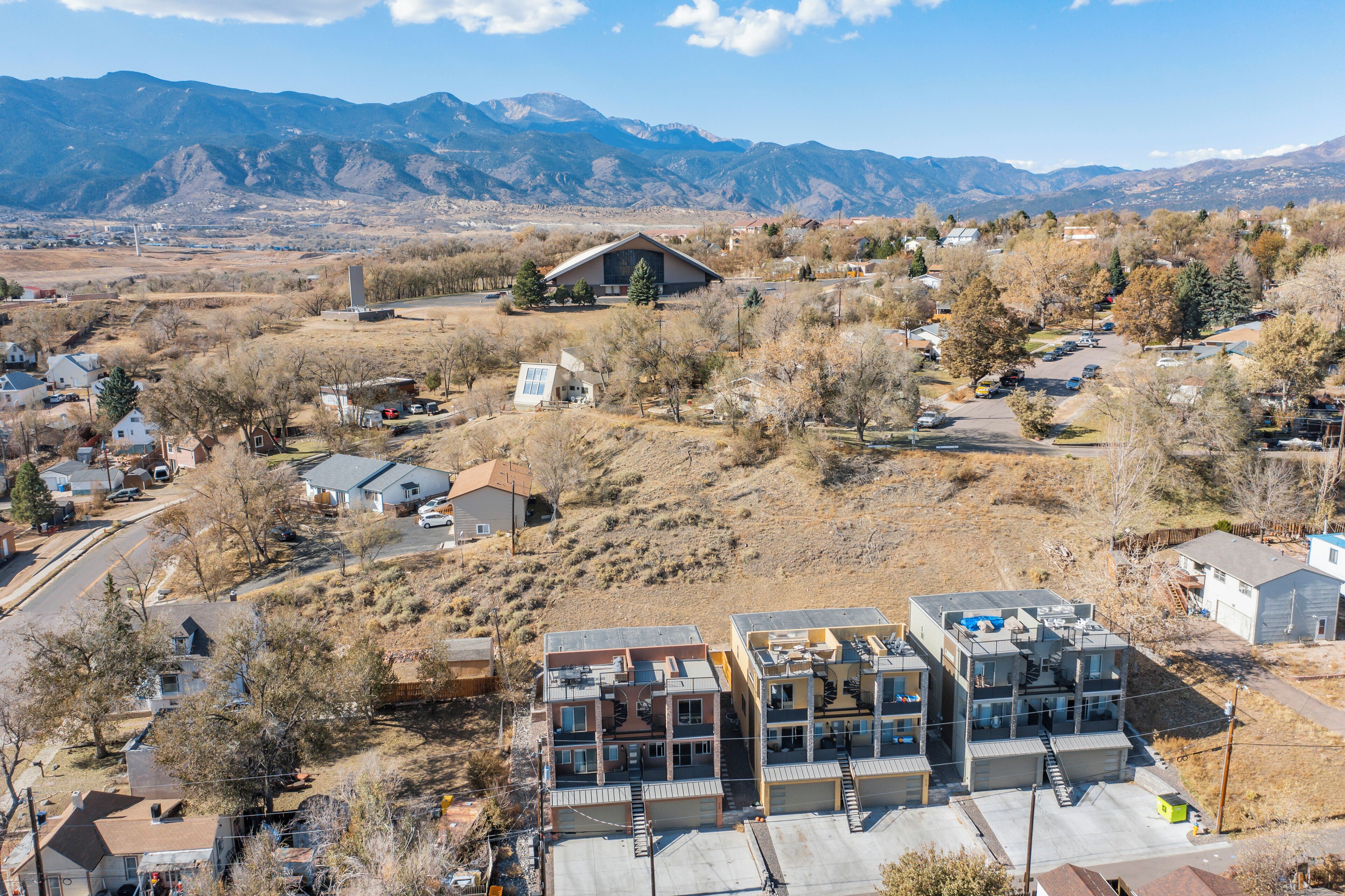A residential area with modern houses, a large building with a sloped roof, and mountains in the background.