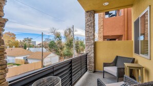 Un balcón con mobiliario de mimbre, un pilar de piedra y vistas a casas vecinas.