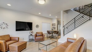 Una sala de estar moderna con sofás de cuero, una mesa de centro de vidrio, un televisor de pantalla plana y una escalera.