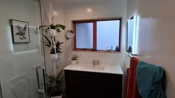 Ein Badezimmer mit Duschkabine aus Glas, einem weißen Waschbecken, einem Fenster und einem Handtuchhalter.