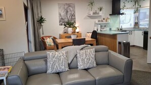A modern living room with a grey sofa, a dining area with a wooden table, and a kitchen with white cabinets and a black countertop. - Townhouse Haven - Modern, Spa, close to Nelson Central! Pets welcome. (Nelson)