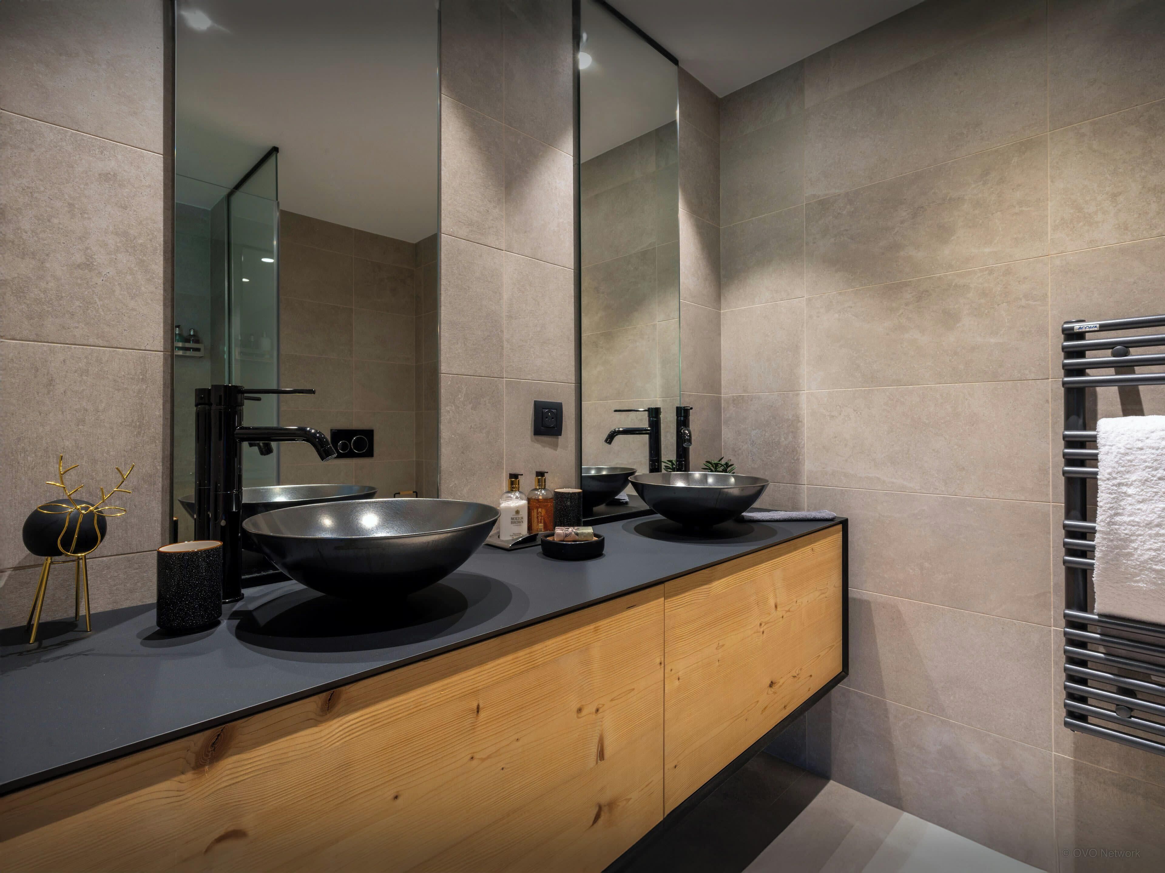A modern bathroom with a large mirror, two black sinks, and a wooden vanity.
