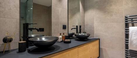 A modern bathroom with a large mirror, two black sinks, and a wooden vanity.