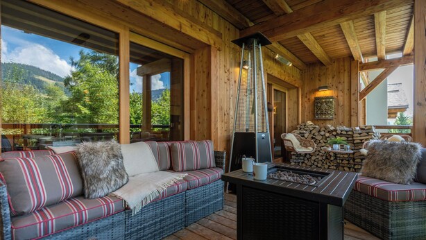 Una terraza de madera con un sofá de mimbre, una mesa y una chimenea.