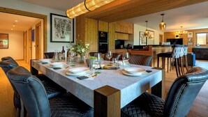 Comedor con una larga mesa dispuesta para seis personas, rodeada de sillas de cuero, techo de madera y una lámpara colgante moderna.