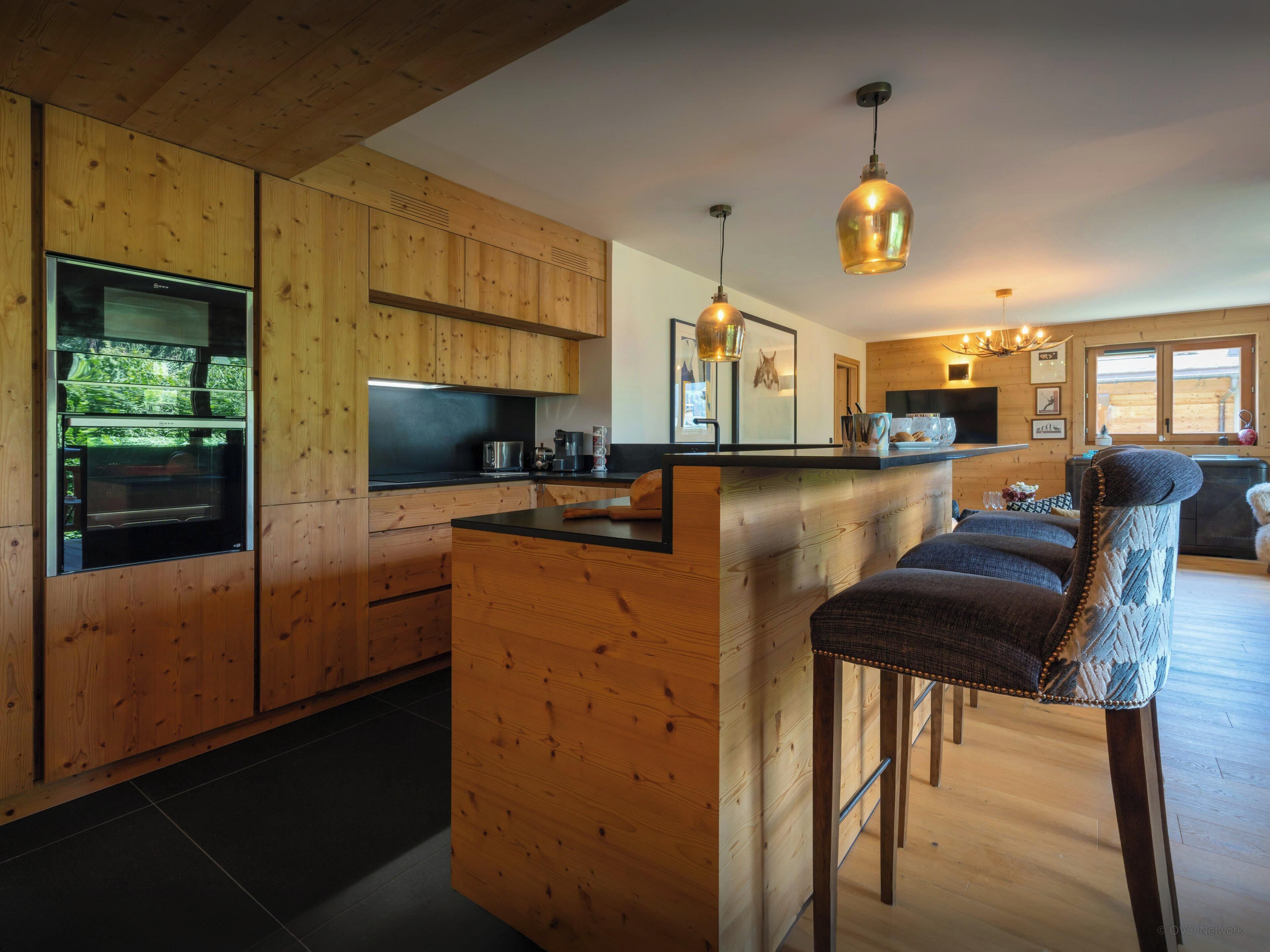 Eine moderne Küche mit Holzschränken, einem eingebauten Ofen und einer Theke mit Barhocker.