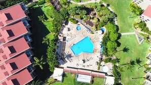 Ein Luftbild eines Resorts mit Schwimmbad, Palmen und einem Gebäude mit roten Dächern.