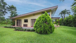 Uma casa moderna de dois andares com telhado plano, cercada por vegetação exuberante e um gramado bem cuidado.