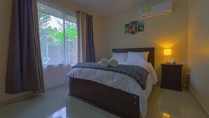 Quarto de hotel com uma cama, uma mesa de cabeceira com abajur e um ar condicionado na parede.