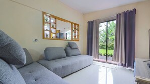 Sala de estar com sofá cinzento, espelho com moldura de madeira e porta de vidro deslizante para um jardim.