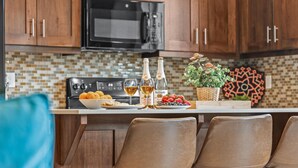 Une cuisine dotée de meubles en bois, d’un four à micro-ondes, d’un plan de travail carrelé, d’une cuisinière et d’un coin bar avec des tabourets.
