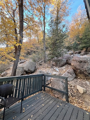 Eine Holzterrasse mit einer Bank, umgeben von Herbstlaub und großen Felsen.