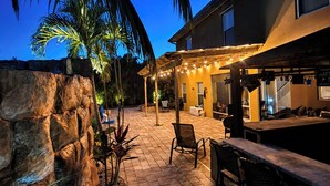 A patio area with a stone wall, palm trees, and outdoor seating. - Resort Style Tranquil Oasis in Beautiful Port Saint Lucie , Florida (Port St. Lucie)