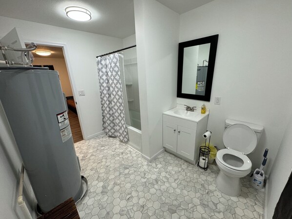 A bathroom with a hexagonal tile floor, a white sink with a mirror above it, a toilet, and a shower curtain. - Central ICT.C (Wichita)