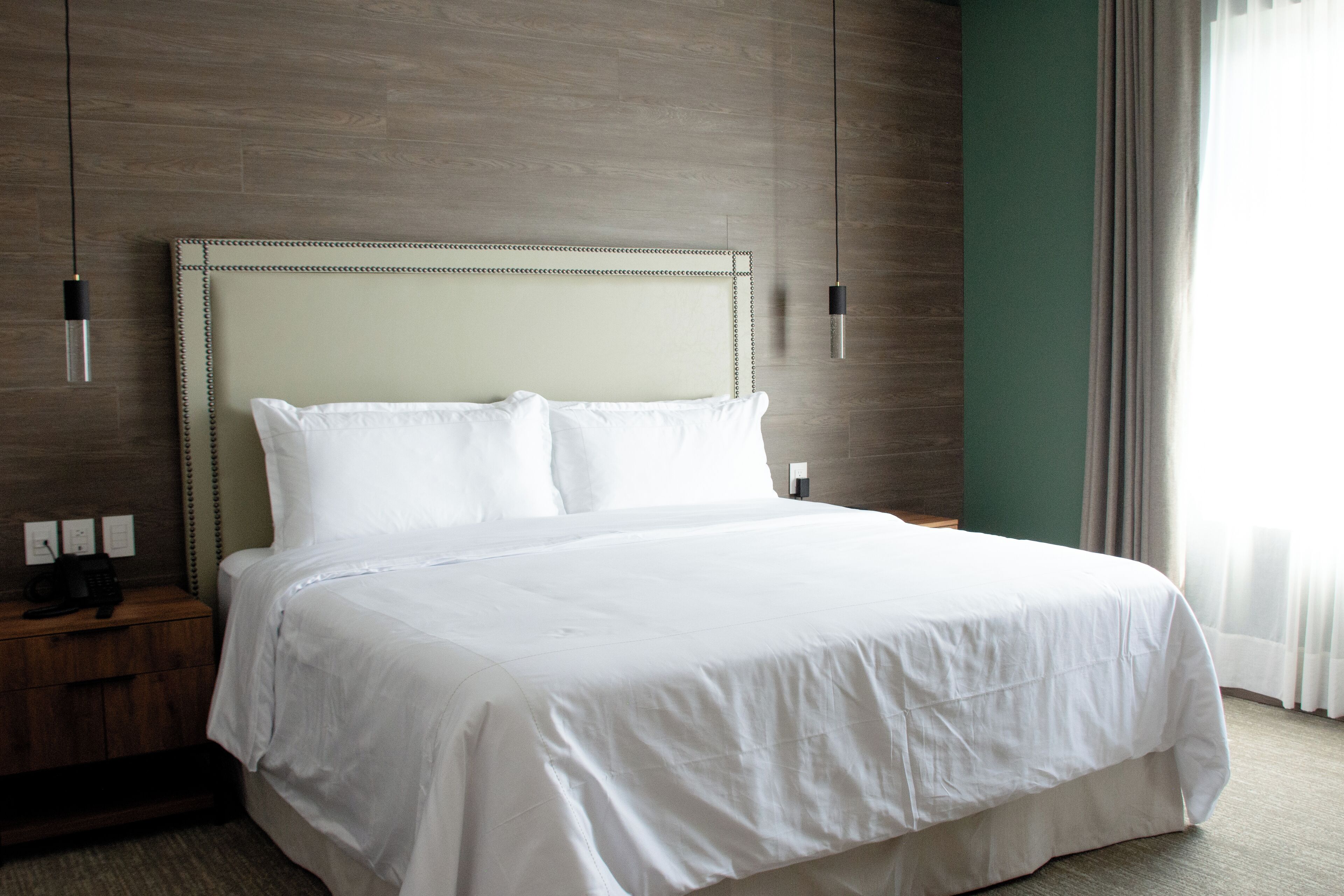 Una cama bien hecha con sábanas blancas en una habitación de hotel con suelo de madera y una pared de acento verde.