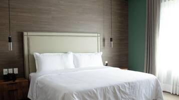 Una cama bien hecha con sábanas blancas en una habitación de hotel con suelo de madera y una pared de acento verde.