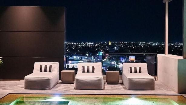Un área de piscina en la azotea con cuatro sillas reclinables y vistas a un paisaje urbano nocturno.