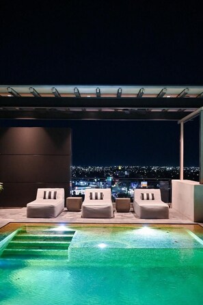 A rooftop pool area with four lounge chairs and a view of a cityscape at night. - Moka Boutique Hotel (Torreón)