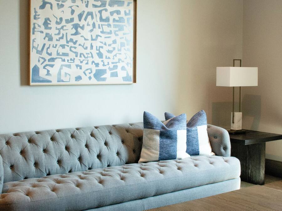 Sala de estar con un sofá capitonado, una mesa de centro, una lámpara y una obra de arte en la pared.