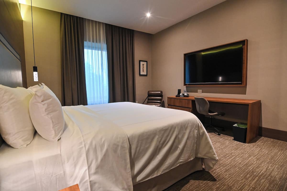 A hotel room with a large bed, a desk, a chair, a television, and a window with curtains.