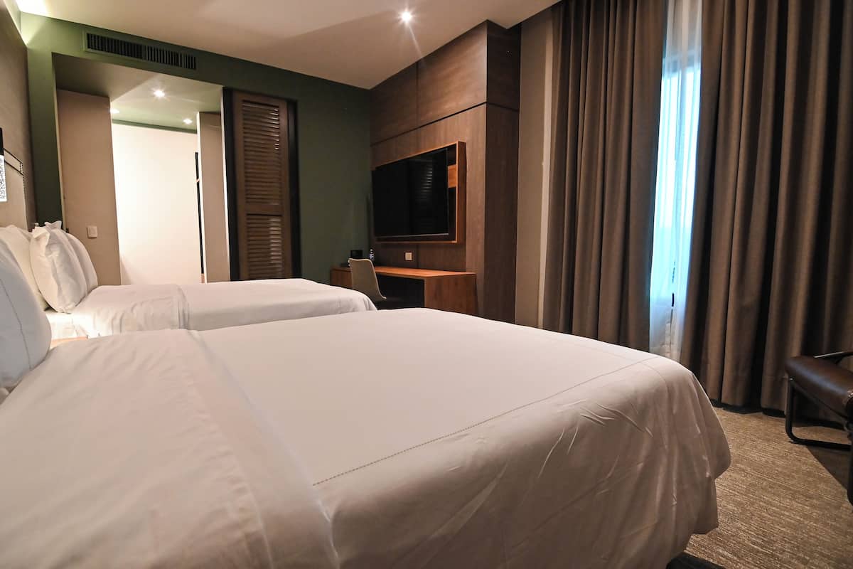 A hotel room with two beds, a TV mounted on the wall, a desk, and a chair.