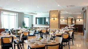 Un comedor bien iluminado con varias mesas dispuestas para el servicio, con sillas de mimbre y un diseño moderno y limpio.