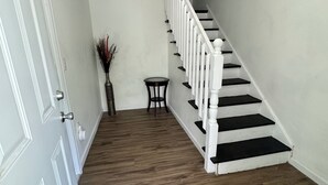A staircase with white railings and dark steps, leading to a landing with a small table and a vase of dried plants. - Central ICT.B (Wichita)