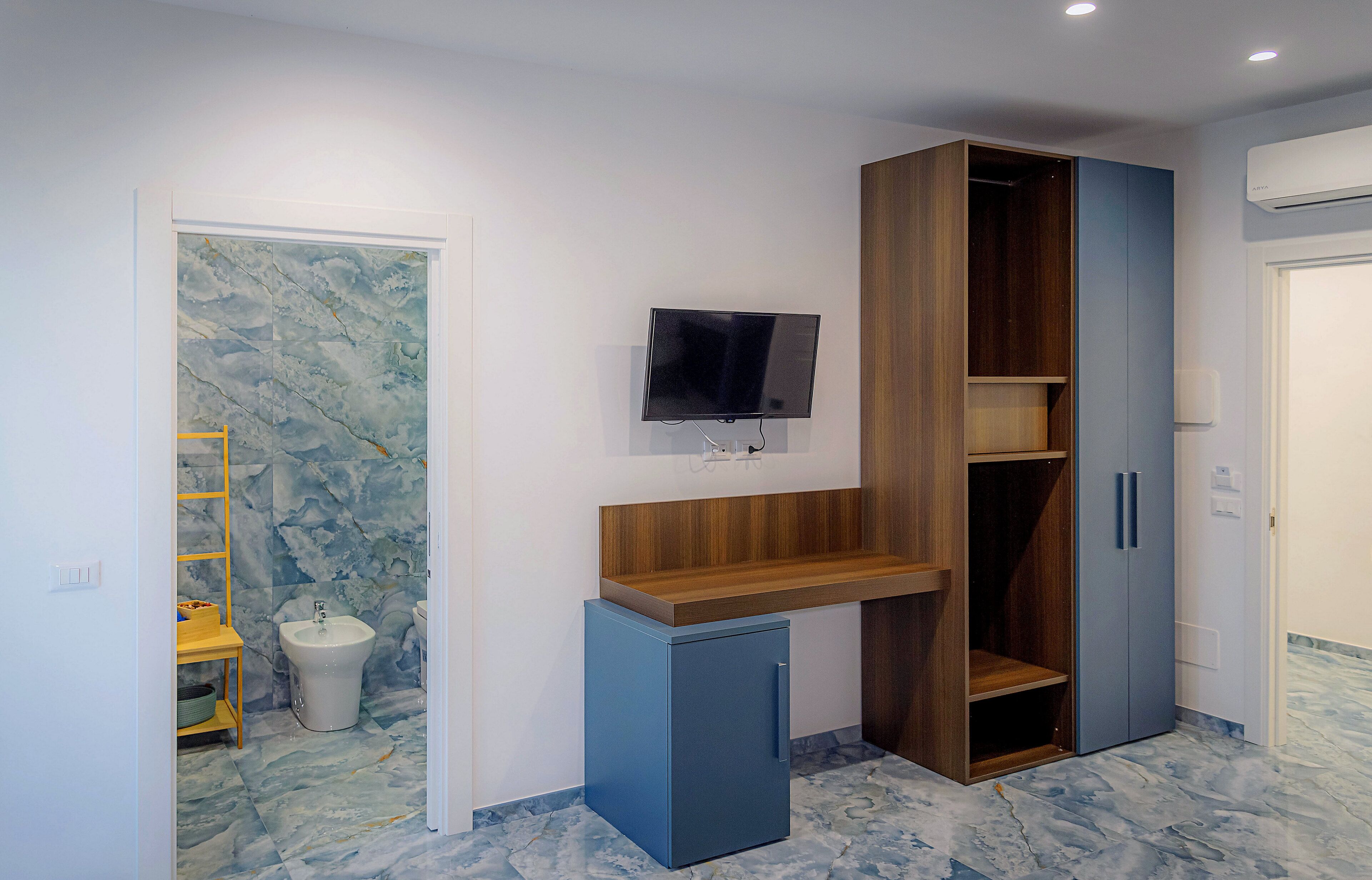 A compact room with a built-in desk, a television, a small refrigerator, and a wardrobe.
