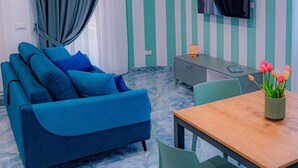 A modern room with a blue sofa, a wooden dining table, and a TV mounted on the wall. - Maison Matie B&B Ercolano (Ercolano)