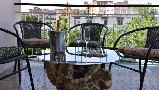 A round glass table with metal chairs and cushions on a balcony with a view of buildings and trees. - Maison Matie B&B Ercolano (Ercolano)