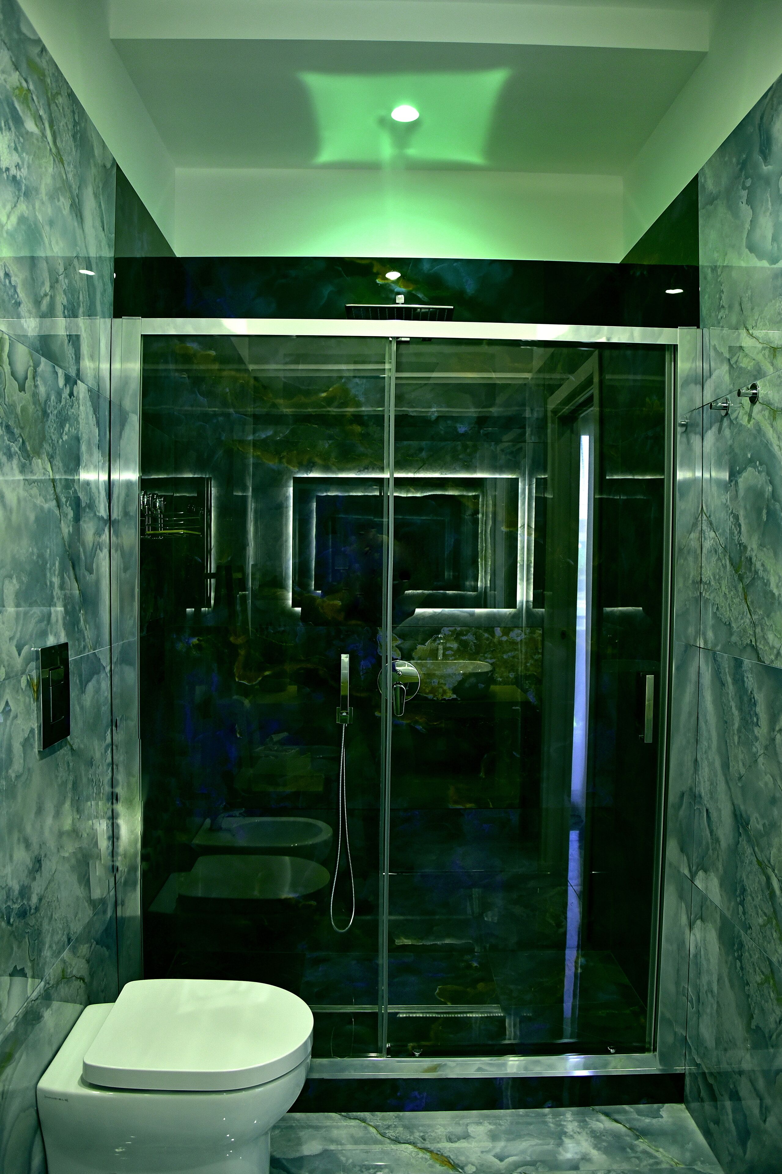 A modern bathroom with a glass-enclosed shower, a toilet, and marble walls.