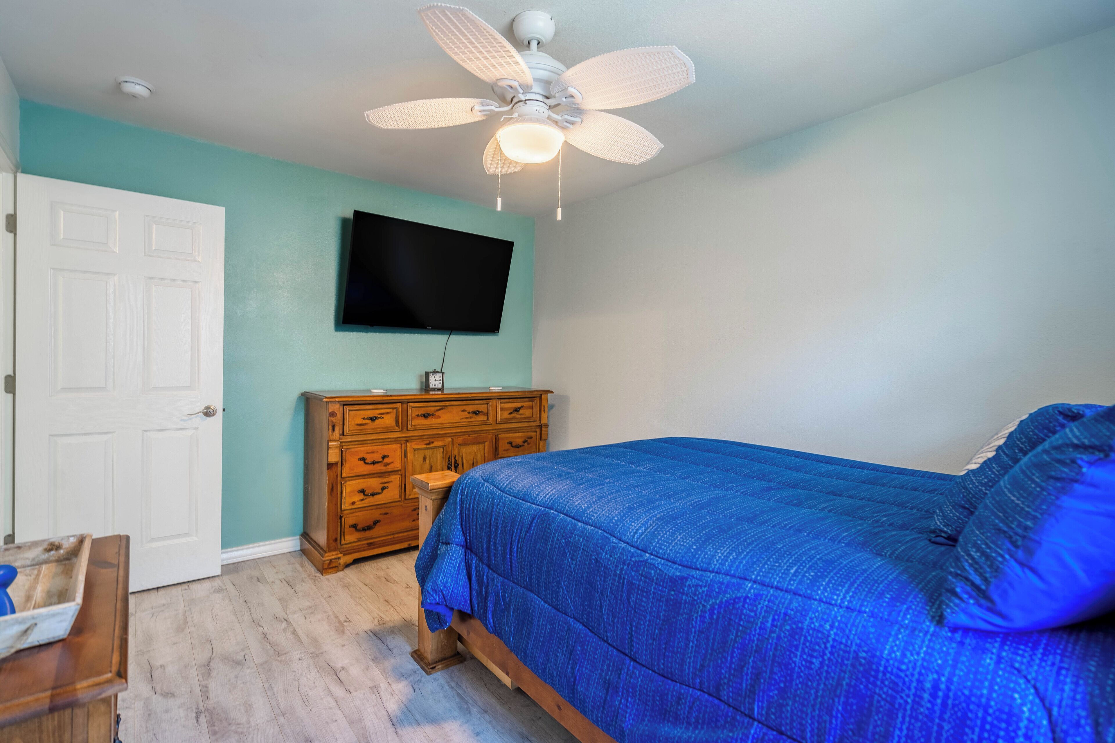 Un dormitorio con cama, cómoda de madera, ventilador de techo y televisor montado.