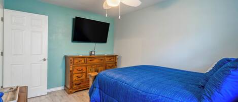Un dormitorio con cama, cómoda de madera, ventilador de techo y televisor montado.