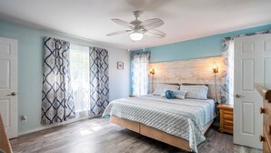 Une chambre à coucher avec un lit, un ventilateur de plafond, une tête de lit en bois et une table de chevet avec une lampe.