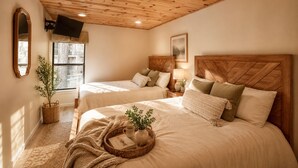 A bedroom with two beds, wooden ceiling, a large window, and a mirror.