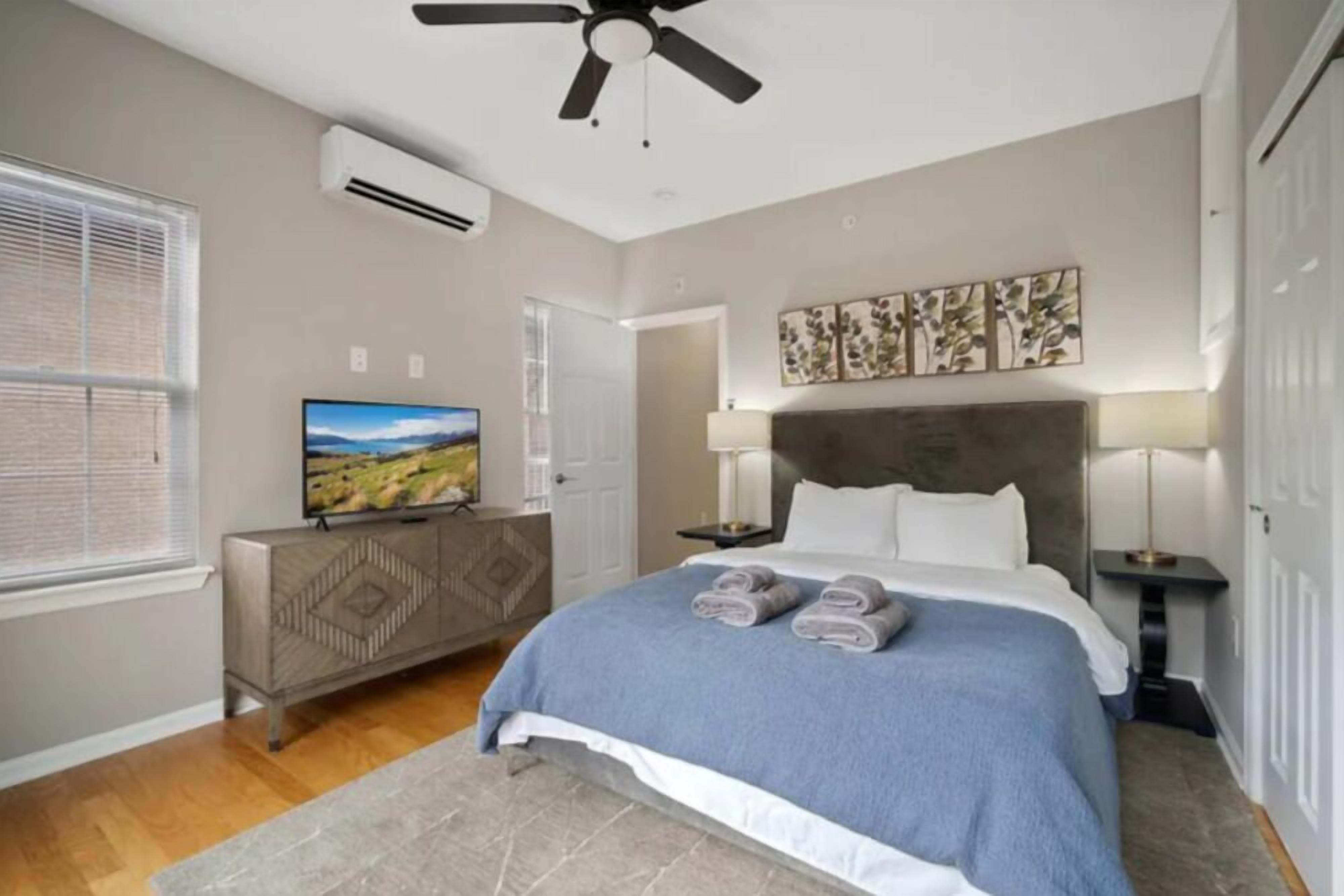Una camera da letto con un letto, una TV sopra un comò, una ventola a soffitto e opere d'arte al muro.