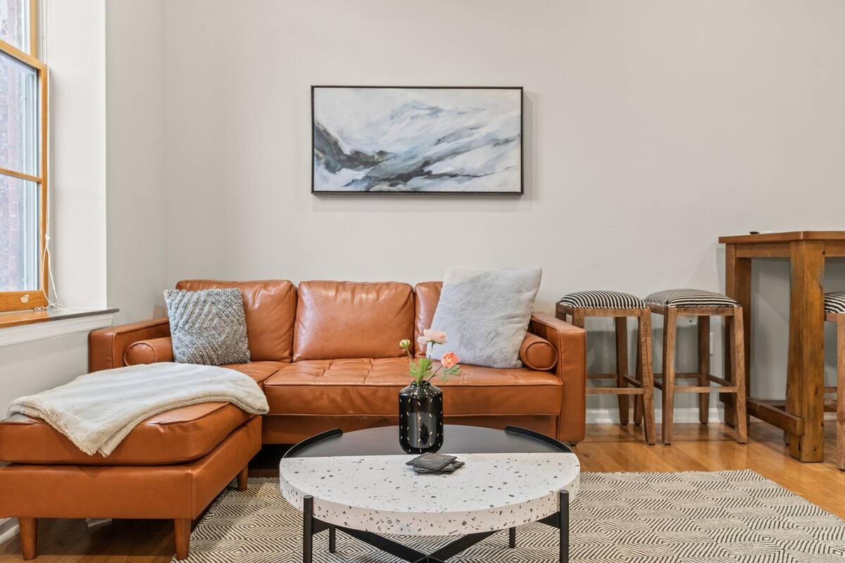 A living room with a brown leather sofa, a round coffee table, and a framed abstract painting on the wall.