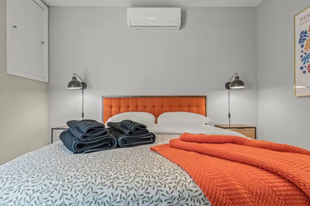 Une chambre d’hôtel avec un lit, deux lampes de chevet, un climatiseur et un tableau encadré au mur.