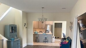 A spacious living area with a wooden floor, a blue sofa, a pet bed, and a kitchen in the background. - Pleasant 4-bedroom house in New Roads with WiFi. (New Roads)
