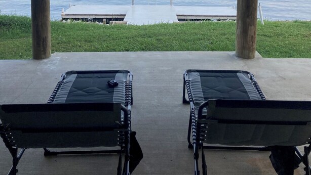 A covered outdoor seating area with two lounge chairs facing a lake. - Pleasant 4-bedroom house in New Roads with WiFi. (New Roads)