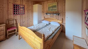 A wooden-paneled bedroom with a single bed, a chair, a small table, and a wall-mounted shelf.