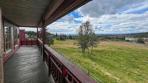 A wooden deck with a view of a grassy field and distant buildings.