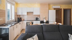 Una cocina moderna con armarios blancos, una zona de comedor con sofá oscuro y un amplio ventanal que proporciona luz natural.