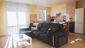Una sala de estar con sofá, mesa de comedor y área de cocina con armarios y electrodomésticos.