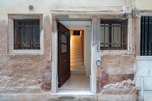 A doorway leading to a staircase with a metal gate on the left and a window with a metal grille on the right. - San Beneto (Venezia)