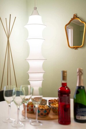Ein Esstisch mit Weingläsern, einer Flasche Rotwein und einer grünen Flasche, möglicherweise Champagner, einer dekorativen Leuchte und einem Spiegel an der Wand.